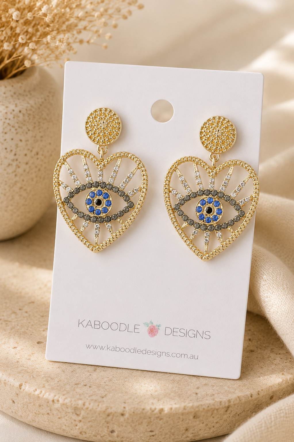 Gold evil eye heart earrings with rhinestone detail displayed on Kaboodle Designs card