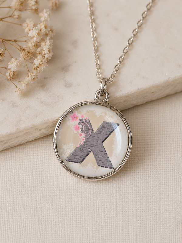 Round resin pendant necklace with grey letter X and pink cherry blossom detail, silver chain