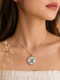 Letter X pendant necklace worn on model's neckline, close-up front view