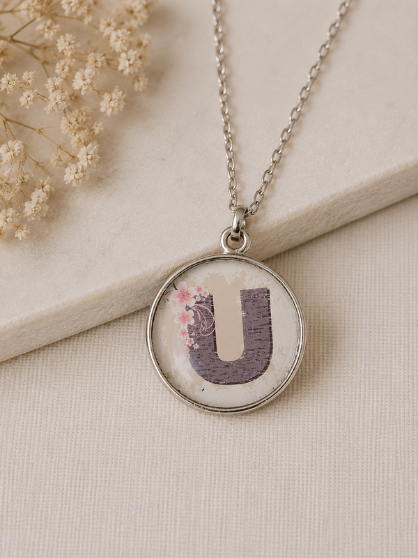 Round silver-toned pendant necklace with distressed letter U and pink floral detail under glossy resin