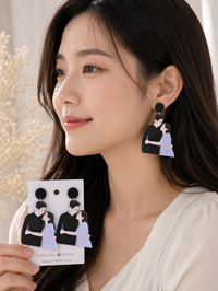 Close-up of Kdrama drop earring worn on ear, showing illustrated couple design and black stud top