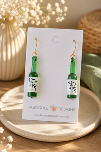 Green soju bottle resin drop earrings on card, showing bottle label detail