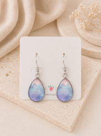 Two purple and blue watercolour teardrop earrings on a stainless steel hook, displayed on a card