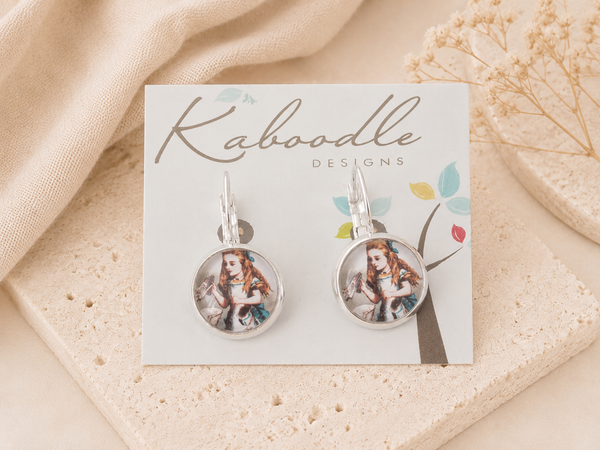 Pair of round Alice in Wonderland earrings on Kaboodle Designs card, showing Alice holding a bottle