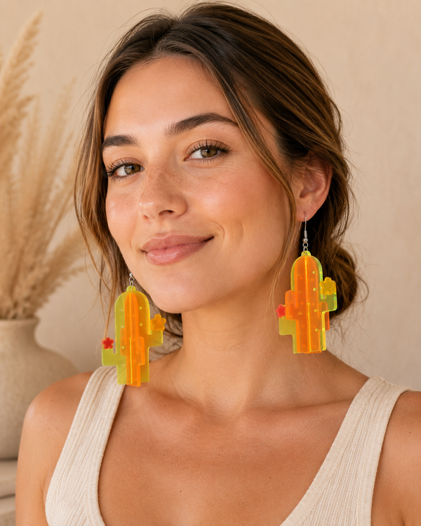 Woman wearing large orange and yellow acrylic cactus drop earrings with flower details