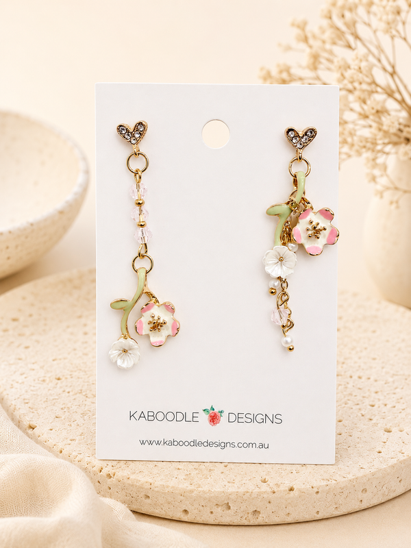 Gold-tone floral drop earrings on card with crystal heart studs, pink and white flower charms and green stem detail