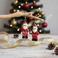 Santa brick earrings hanging from a wooden branch with gold ribbon and pinecones
