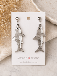 Pair of marbled grey and white shark-shaped dangle earrings with silver ball-top studs, displayed on a card.