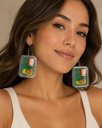 Close-up of a model wearing avocado punnet dangle earrings, showing the sliced avocado detail and price sticker on each