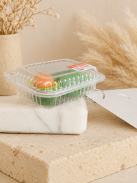 Close-up of a single avocado punnet earring resting on a marble block, showing the sliced avocado and clear ridged tray