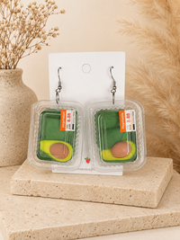 Pair of avocado punnet dangle earrings on a display card, showing sliced avocado inside clear plastic trays with price