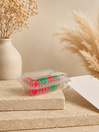 Single strawberry punnet earring charm resting on a stone surface, showing the clear container with red and green fruit