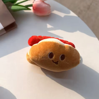 Plush hot dog keychain with smiling embroidered face resting on a table