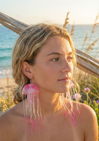 Close-up of woman wearing long pink jellyfish earring, showing spotted dome and trailing tentacles against her shoulder