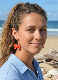 Close-up of a woman wearing one orange resin crab earring, styled at the beach