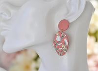 Close-up of coral floral drop earring worn on ear, showing painted stem and petal detail