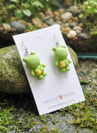 Frog and duck drop earrings displayed upright against mossy rock background