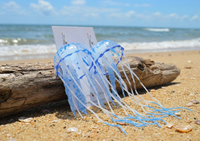 Close-up of blue jellyfish earrings on a card showing tentacle detail and beach background
