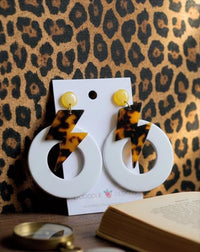Tortoiseshell lightning bolt and white hoop earrings on card against leopard print backdrop