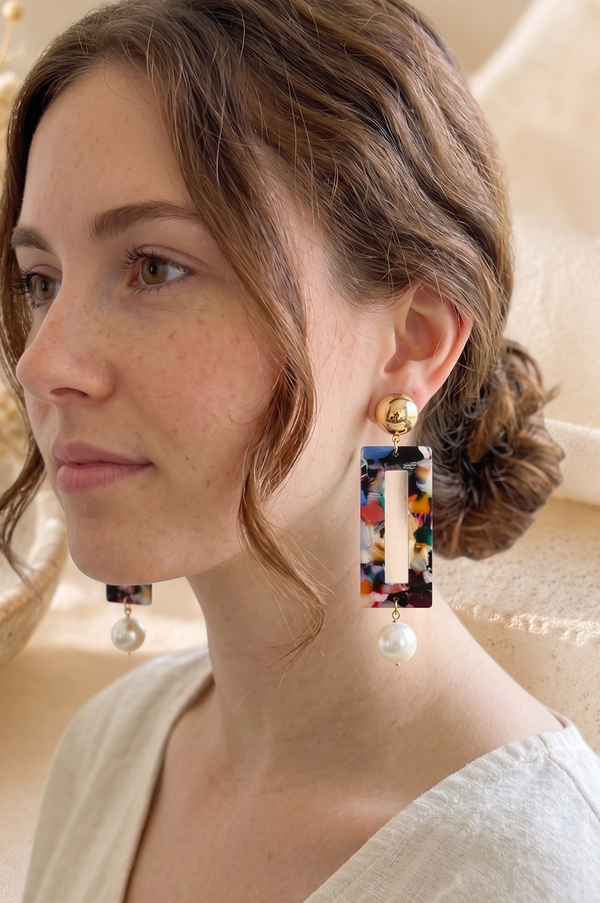 Close-up of marbled acetate earring worn on ear showing open rectangle cutout and pearl drop