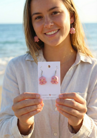 Pink octopus earrings worn on a smiling woman at the beach, close-up on ears