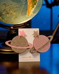 Pink and multi-glitter Saturn drop earrings with star studs on a Kaboodle Designs card, globe in background