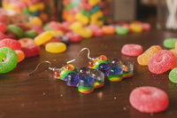 Close-up of rainbow gummy bear earrings laid on a table surrounded by sour lolly rings