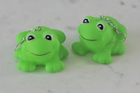 Two green plastic frog earring charms side by side on a marble surface, front-facing
