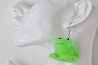 Close-up of single green frog earring hanging from a mannequin ear, showing silver hook detail