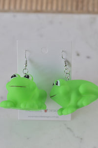 Pair of green plastic frog drop earrings on a Kaboodle Designs display card
