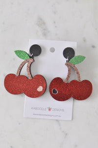 Pair of glitter red cherry drop earrings with green leaves on Kaboodle Designs card