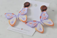 Top-down view of two butterfly drop earrings with wings spread, resting on Kaboodle Designs card