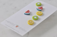 Close-up angled view of watermelon, lemon and kiwi stud earrings showing glossy finish