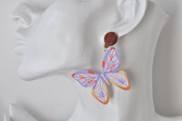 Close-up of acrylic butterfly earring worn on ear showing stained-glass wing pattern and brown stud top
