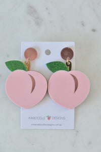 Pink perspex peach drop earrings with green glitter leaf on Kaboodle Designs card