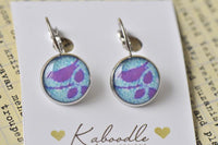 Round clip-on dangle earrings with purple bird motif on teal patterned background, silver frame
