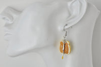 Close-up of peanut butter toast earring with knife charm worn on ear