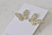 Angled close-up of gold butterfly earrings highlighting sparkle and detailed wing pattern