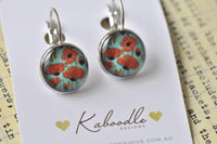 Round clip earrings with red poppy print on teal background, silver plated frame, front view