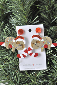 Acrylic Christmas earrings on card showing sloth in Santa hat holding candy cane, with red glitter studs
