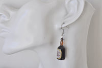Whisky bottle drop earring worn on ear, showing scale and dangle length