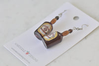 Close-up of whisky bottle earrings lying flat showing glossy resin bottle shape and label