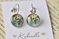 Round clip-on dangle earrings with blue and yellow floral cabochon design on Kaboodle card