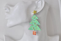 Close-up of Christmas tree earring worn on ear model showing glitter finish and dangling present charm