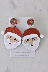 Pair of Santa Claus drop earrings with glitter red hats and confetti studs on card