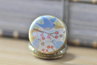 Close-up of the bluebird trio and cherry blossom design on the pocket watch pendant