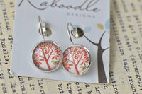 Round clip-on earrings with red tree and bird design on silver setting, close-up on branded card
