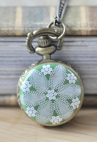 Bronze pocket watch necklace with green and white lace doily design on the front cover