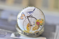 Close-up of the penny farthing, bird and butterfly artwork on the pocket watch pendant