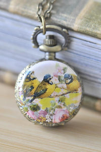 Bronze pocket watch necklace with a trio of yellow birds and pink floral artwork on the case front